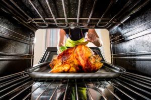 Woman placing turkey in an oven.